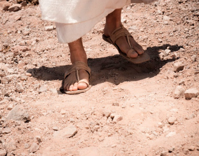 Foto dos pés de um homem de sandálias caminhando no deserto