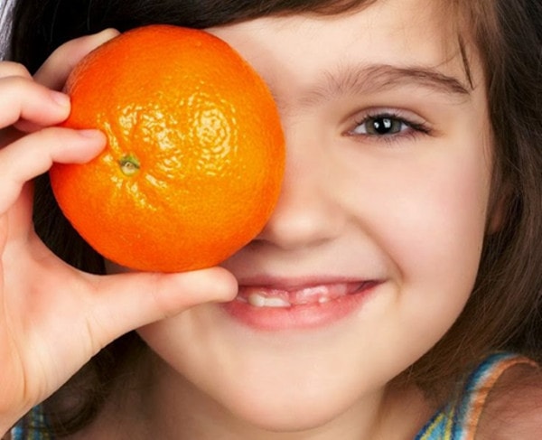 Foto de menina brincando com uma laranja sobre seu rosto