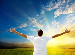 Fotografia de um homem de costas de braços abertos saudando o nascer do sol no horizonte.