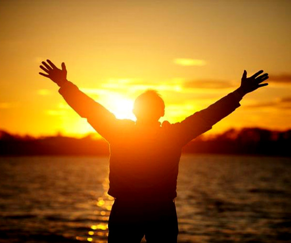Foto - homem abrindo os braços diante de um nascer do sol
