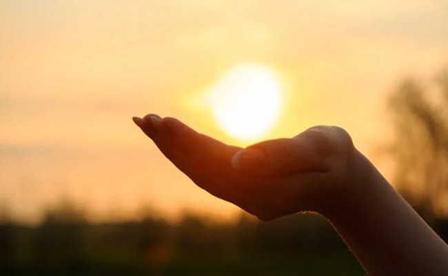 Foto de mão em gesto de gratidão, tendo acima de si a luz do sol
