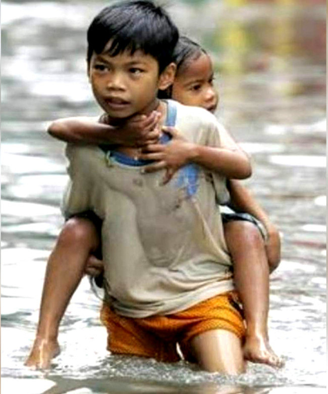 Foto de uma criança carregando outra nas costas em meio a uma enchente